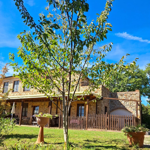 Stone house with a lush garden and tree at Agriturismo & Glamping Serraiola Alta, Tuscany, Italy.