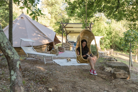Kvinde slapper af i hængestol foran glampingtelt hos Agriturismo & Glamping Serraiola Alta i Toscana.