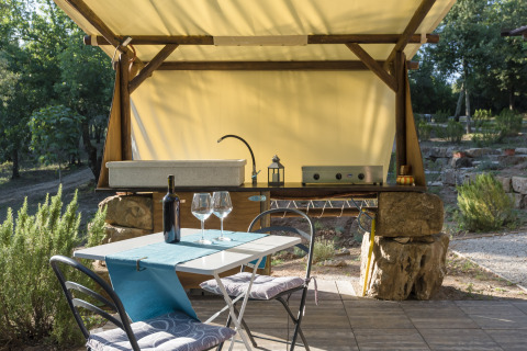 Cuisine extérieure de glamping avec évier, table dressée, bouteille de vin et verres dans la nature toscane.