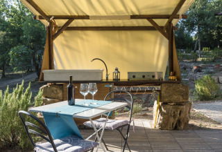 Cucina glamping all’aperto con lavandino, tavolo apparecchiato, vino e bicchieri immersi nella natura toscana.