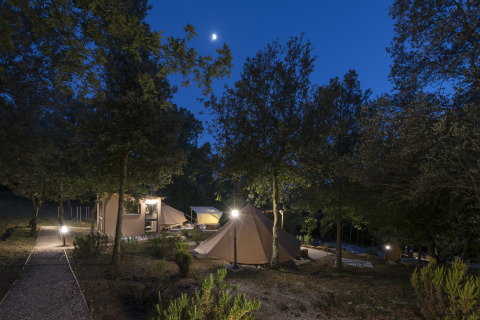 Glampingområdet Serraiola Alta i Toscana om natten med oplyste telte under træer og en klar himmel.