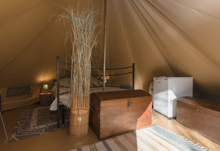 Indvendig visning af et luksuriøst glampingtelt med seng, kiste, minikøleskab og rustikke dekorationer.