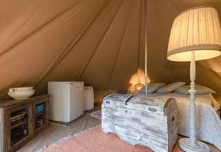 Gemütliches Glampingzelt mit Bett, Stehlampe, Kommode und Kühlschrank bei Serraiola Alta in der Toskana.