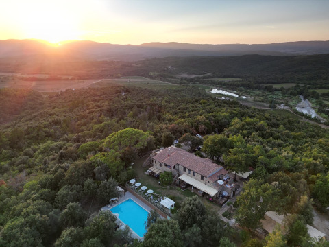 Aerial view of Agriturismo & Glamping Serraiola Alta in Tuscany with pool, surrounded by forest at sunset.