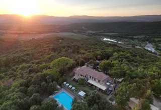 Luchtfoto van Agriturismo & Glamping Serraiola Alta in Toscane met zwembad, omgeven door bos bij zonsondergang.