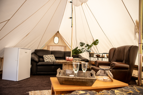Interior of a glamping tent with leather sofa, fridge, and plants at Landgoed Lindehof – Glamp Lodges Friesland.