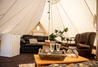 Interior of a glamping tent with leather sofa, fridge, and plants at Landgoed Lindehof – Glamp Lodges Friesland.