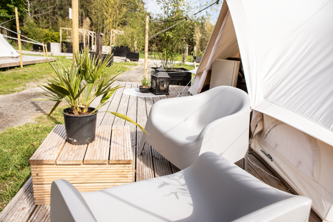 Outdoor deck with modern chairs, potted plant, and tent at Landgoed Lindehof – Glamp Lodges Friesland, Netherlands.
