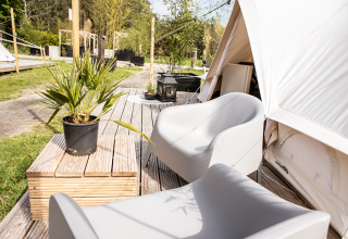 Outdoor deck with modern chairs, potted plant, and tent at Landgoed Lindehof – Glamp Lodges Friesland, Netherlands.
