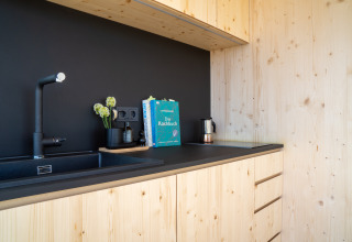 Moderne kitchenette in lichte houtsoort bij Ostsee Baumhaus aan de Oostzee met zwarte spoelbak en decoratie.