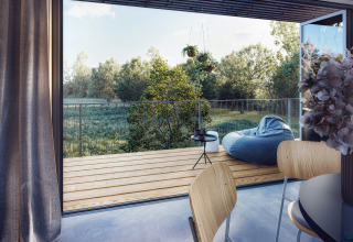 Alloggio glamping moderno Ostsee Baumhaus con terrazza in legno, pouf e vista sulla natura verde.