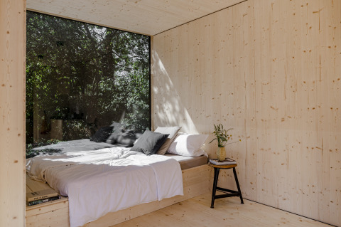 Minimalistische houten slaapkamer met groot raam, bed en uitzicht op groen in Oostzee boomhut glamping.