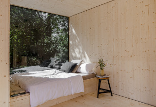 Minimalistische houten slaapkamer met groot raam, tweepersoonsbed en natuurzicht in Ostsee boomhut glamping.