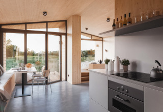 Modernes Glamping-Ostsee-Baumhaus mit großen Fenstern, heller Holzeinrichtung und Küche in Schleswig-Holstein.