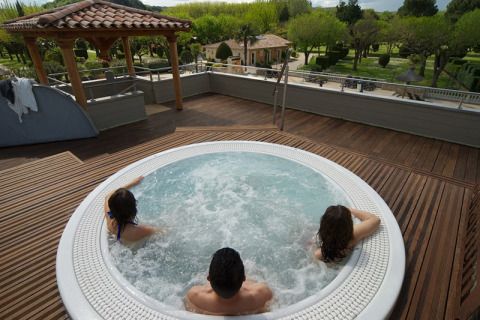 Tre personer slapper af i jacuzzi på en træterrasse hos Camping Nature Parc l'Ardéchois med naturskøn udsigt.