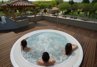 Tre personer slapper af i jacuzzi på en træterrasse hos Camping Nature Parc l'Ardéchois med naturskøn udsigt.