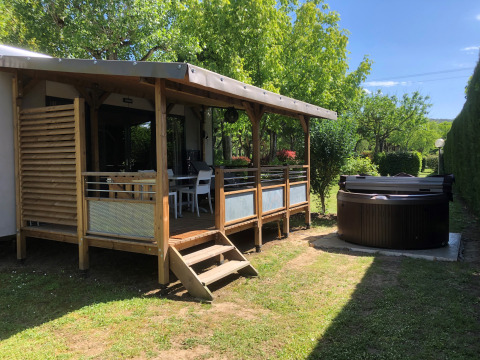 Glamping på Camping Nature Parc l'Ardéchois med en overdækket terrasse og jacuzzi i en grøn have.