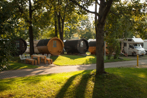 Alojamiento glamping en Stuttgart Cannstatter Wasen con barriles de vino y autocaravanas entre árboles.