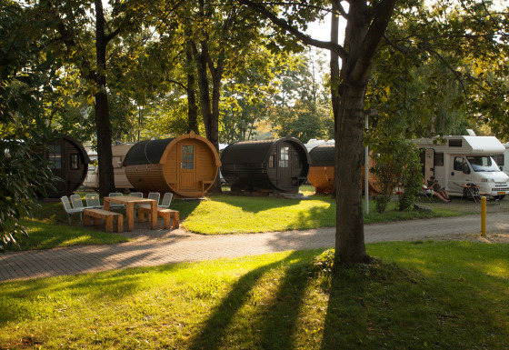 Alojamiento glamping en Stuttgart Cannstatter Wasen con barriles de vino y autocaravanas entre árboles.
