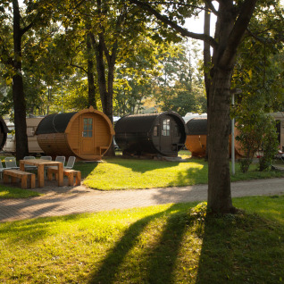 Hébergement glamping à Stuttgart Cannstatter Wasen avec cabanes en fûts de vin et camping-cars sous arbres.