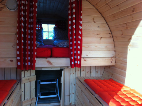 Binnenzicht van glamping in Stuttgart Cannstatter Wasen met rode kussens en gordijnen met stippen.