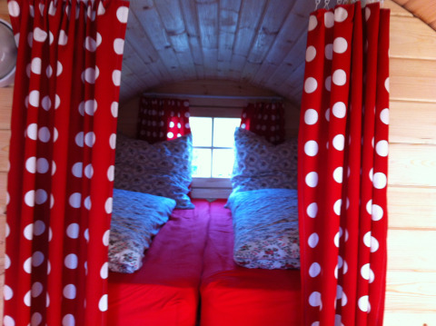 Binnenzicht van glamping accommodatie in Stuttgart Cannstatter Wasen met rode gordijnen en gezellige bedden.