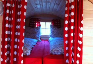 Interior view of glamping accommodation in Stuttgart Cannstatter Wasen with red curtains and cozy beds.