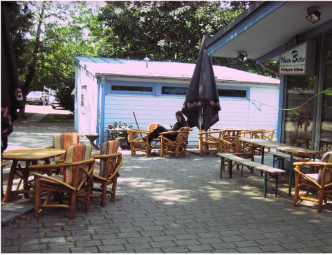 Udendørs caféområde ved Camping Stuttgart Cannstatter Wasen med træmøbler og parasoller i Baden-Württemberg.