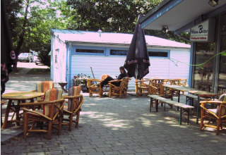 Zona de cafetería al aire libre en Camping Stuttgart Cannstatter Wasen con sillas y sombrillas de madera en Baden-Württemberg.