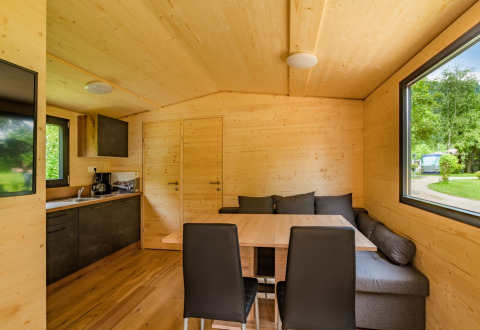 Sistemazione glamping moderna con interni in legno, zona pranzo, divano e grandi finestre al Drau Camping Sachsenburg.