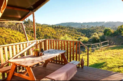 Terrasse en bois avec vue sur collines verdoyantes à Quinta Vida Verde Glamping Portugal, espace repas rustique.