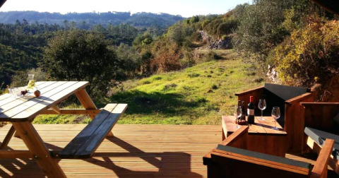 Glamping bij Quinta Vida Verde in Portugal, met terras, picknicktafel, wijn en uitzicht op heuvels en natuur.