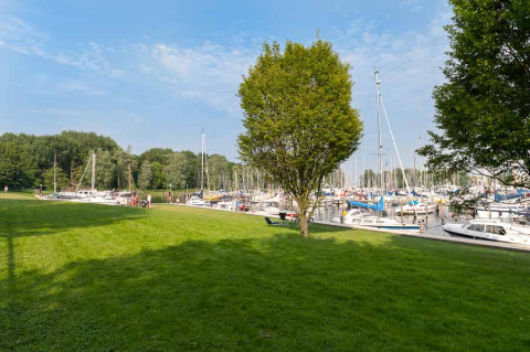 Groen park met bomen naast een jachthaven vol boten bij Marina Parcs Naarden, Noord-Holland, Nederland.