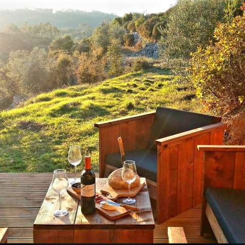 Alojamiento glamping en Portugal con vino, pan y queso en una terraza con vistas a verdes colinas.