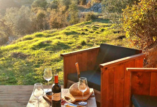 Alojamiento glamping en Portugal con vino, pan y queso en una terraza con vistas a verdes colinas.