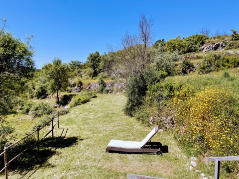 Pradera soleada con tumbona en Quinta Vida Verde Glamping Portugal, rodeada de colinas verdes y naturaleza.