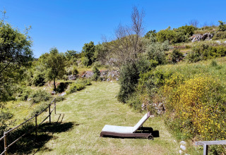 Sonnige Wiese mit Liegestuhl bei Quinta Vida Verde Glamping Portugal, umgeben von grünen Hügeln.