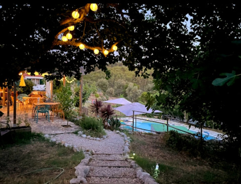 Pad met sfeerverlichting, terras en zwembad bij Quinta Vida Verde - Glamping Portugal in de avondschemer.