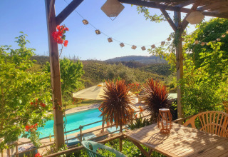 Udsigt fra en terrasse på Quinta Vida Verde Glamping Portugal med pool, grønne bakker og solskin.