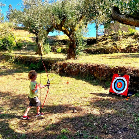 Un enfant s'entraîne au tir à l'arc à Quinta Vida Verde - Glamping Portugal, entouré de verdure.