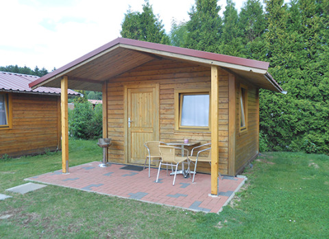 Cabaña de madera con terraza cubierta, barbacoa y sillas en Camping 'Am Leuchtturm' en Baja Sajonia, Alemania.