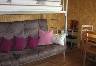Interior of glamping accommodation at Camping 'Am Leuchtturm' with a bunk bed, sofa, table and chairs.