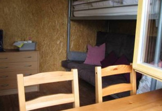 Interior de cabaña glamping con litera, sofá, mesa y sillas de madera en Camping 'Am Leuchtturm' en Baja Sajonia.