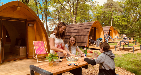 Familie entspannt vor Holz-Pods auf Camping Blauer See Garbsen, umgeben von grüner Natur.