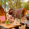Family enjoys outdoor meal in front of wooden pods at Camping Blauer See Garbsen in forest setting.