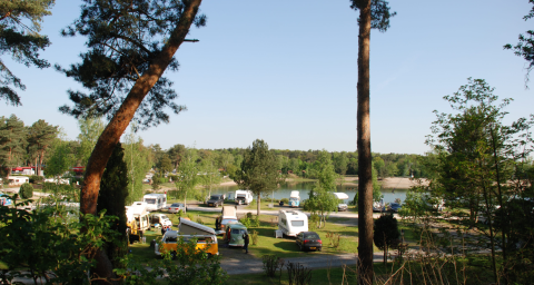 Camping Blauer See Garbsen in Bassa Sassonia con camper, tende, alberi e lago sullo sfondo naturale.