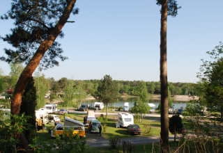Camping Blauer See Garbsen in Niedersachsen mit Wohnmobilen, Bäumen und See im Hintergrund.