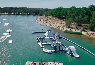 Camping Blauer See Garbsen mit Sandstrand, Wasserpark auf dem See, Baden und Bäumen im Hintergrund.