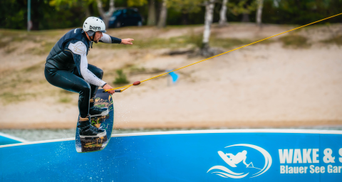 Un wakeboardeur casqué glisse sur un câble à Wake & Ski Blauer See Garbsen, camping en Basse-Saxe.