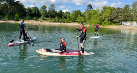 Quattro persone fanno paddle al lago del Camping Blauer See Garbsen - Pods Nedersaksen, circondate dalla natura.
